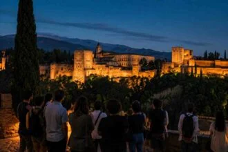 Visitors viewing the illuminated Alhambra at night from a scenic overlook in Granada.